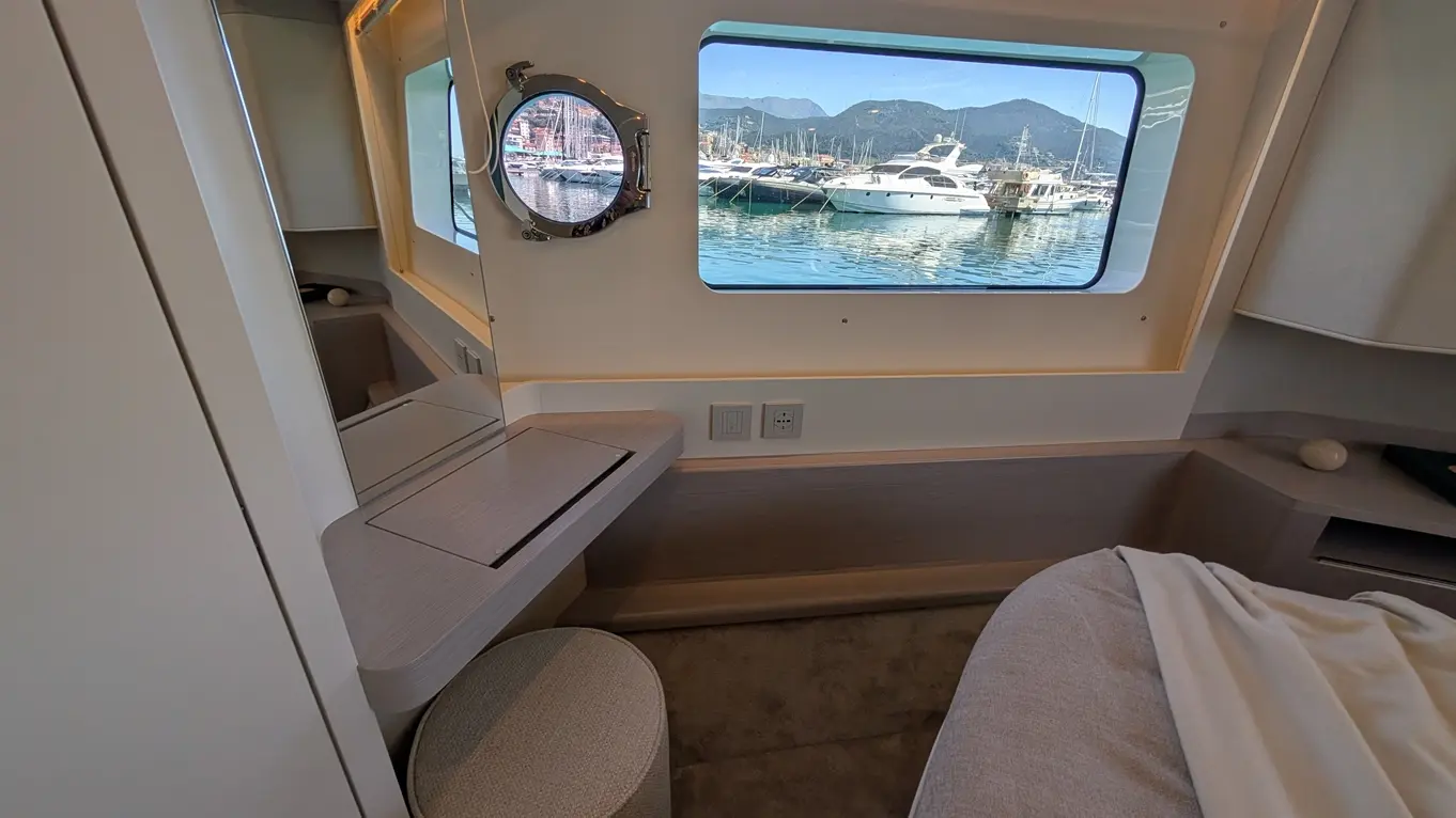 Modern boat interior featuring a round mirror, a desk, and a view of the marina with boats and mountains outside.